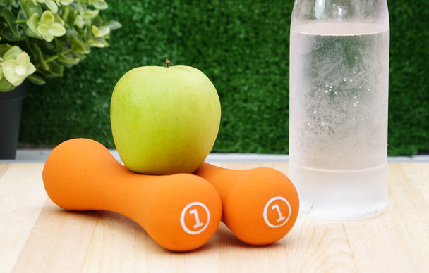Narancs súlyzók zöld alma és üveg vizet fa háttér   - Fotó, kép