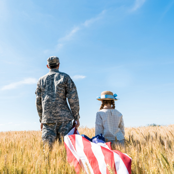back view of soldier and kid standing in field and holding american flag  - Foto, Bild