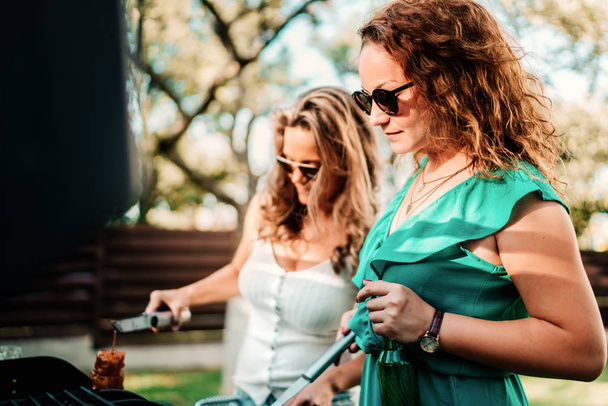 Two woman cooking at barbecue party, having drinks and smiling - Foto, immagini