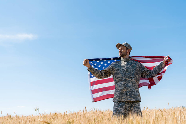 soldier in cap and uniform holding american flag in field  - Photo, Image