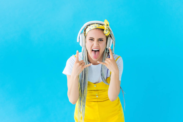 κορίτσι με ράμες στα ακουστικά που προεξέχουν γλώσσα και κάνοντας ροκ σημάδια απομονωμένα σε τυρκουάζ - Φωτογραφία, εικόνα