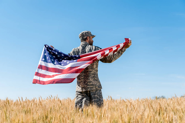 soldier in cap and uniform holding american flag in golden field with wheat  - Foto, imagen