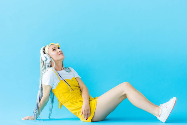 girl with dreadlocks in headphones sitting and looking up on turquoise - Photo, image