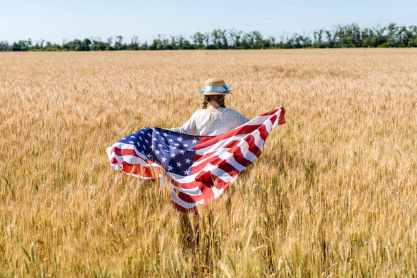 back view of kid holding american flag with stars and stripes in golden field  - Φωτογραφία, εικόνα