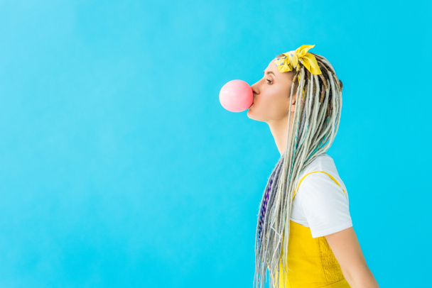 side view of girl with dreadlocks blowing bubblegum isolated on turquoise with copy space - Zdjęcie, obraz
