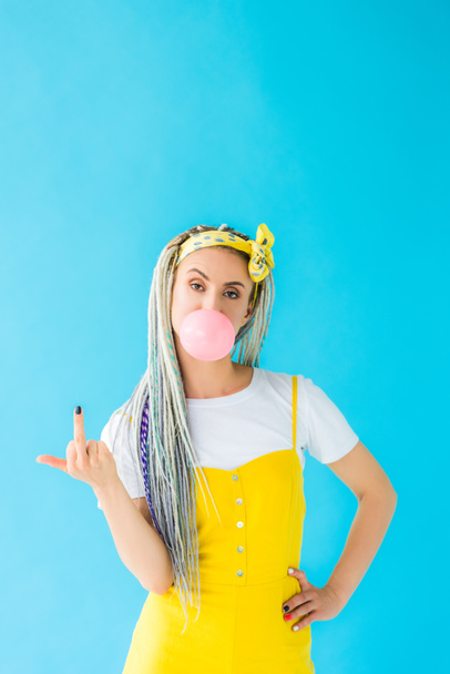 girl with dreadlocks blowing bubblegum and showing middle finger on turquoise - Fotó, kép