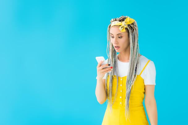 shocked girl with dreadlocks using smartphone isolated on turquoise - Foto, Imagen