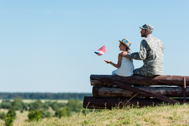 cute child holding american flag near father in military uniform while sitting in fence  - Foto, Imagem