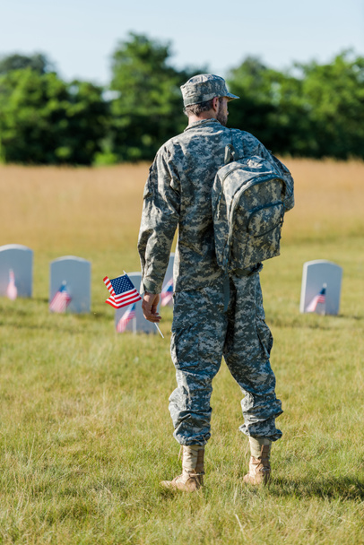 katonai férfi gazdaság amerikai zászló közelében sírkövek a temetőben  - Fotó, kép