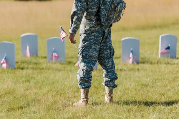 cropped view of military man holding american flag near headstones in graveyard  - Photo, Image