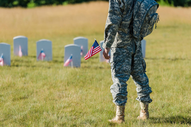 cropped view of soldier holding american flag near headstones in graveyard  - Fotó, kép