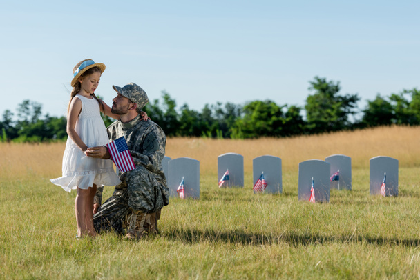 military man in cap sitting near kid in straw hat and headstones in graveyard  - 写真・画像