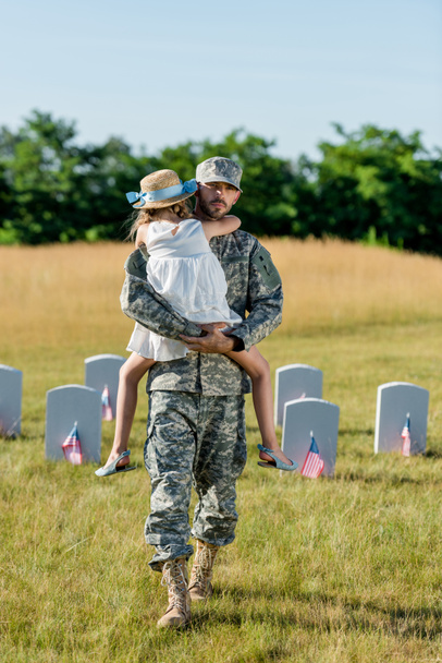veteran in cap holding in ams kid in straw hat near headstones with american flags  - Фото, изображение