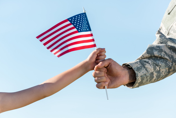 cropped view of military father and daughter holding american flag against blue sky - Fotografie, Obrázek