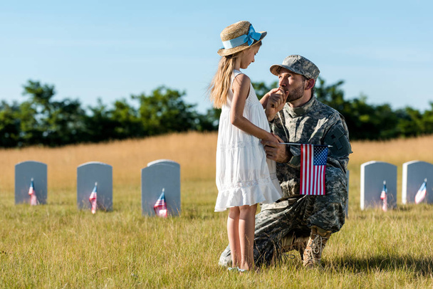 homem militar de uniforme olhando para a filha perto de lápides no cemitério
  - Foto, Imagem