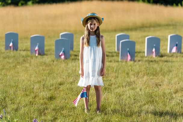 sad kid in white dress standing on graveyard with american flag  - Photo, Image