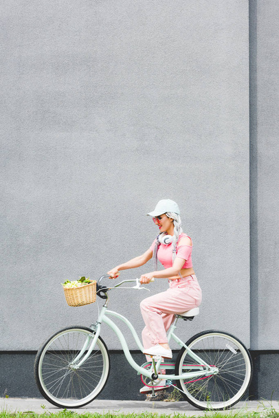 stylish girl riding bicycle near wall with copy space - Photo, Image