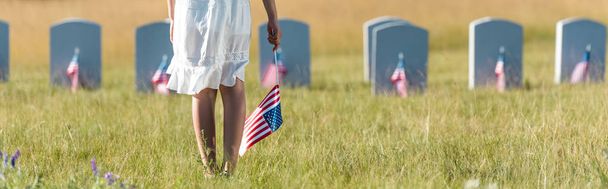 Panoramaaufnahme eines Kindes in weißem Kleid, das mit amerikanischer Flagge auf dem Friedhof steht  - Foto, Bild