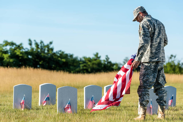 soldier in uniform and cap holding american flag in graveyard  - Zdjęcie, obraz