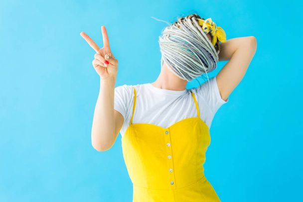 dívka s příšerama zakrývající tvář vlasy a ukazující mírovou známku izolovanou na tyrkysové - Fotografie, Obrázek