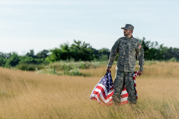 soldaat in camouflage uniform Holding Amerikaanse vlag in gouden veld  - Foto, afbeelding