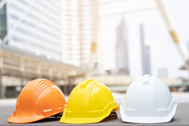 πορτοκαλί, κίτρινο, λευκό σκληρό ασφάλεια φορούν καπέλο κράνος στο έργο στο εργοτάξιο κτίριο σε τσιμεντένιο πάτωμα στην πόλη. κράνος για εργάτη ως μηχανικός ή εργαζόμενος. έννοια ασφάλεια πρώτα - Φωτογραφία, εικόνα
