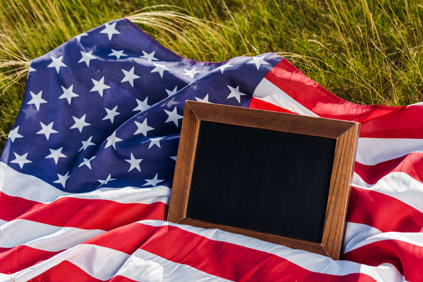 empty chalkboard on american flag with stars and stripes on green grass - Foto, immagini