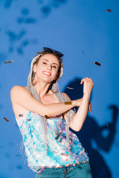 beautiful smiling stylish girl looking at camera on blue with confetti - Valokuva, kuva