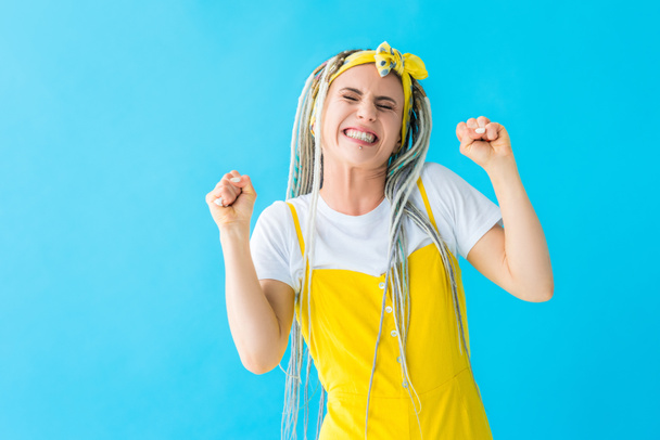 excited girl with dreadlocks cheering with clenched fists isolated on turquoise - Photo, image