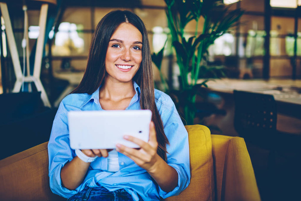 Portrait of cheerful woman dressed in casual apparel looking at camera while waiting for updating on touch pad, positive female blogger using digital tablet for communicate with followers from website - Φωτογραφία, εικόνα
