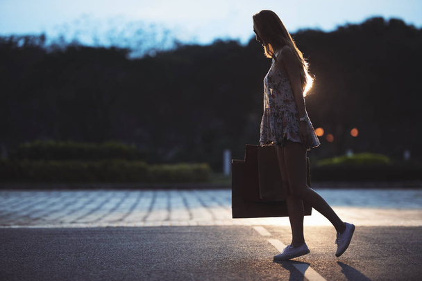 Aydınlatmasız sokakta yürüyen birçok alışveriş poşeti ile genç kadın - Fotoğraf, Görsel