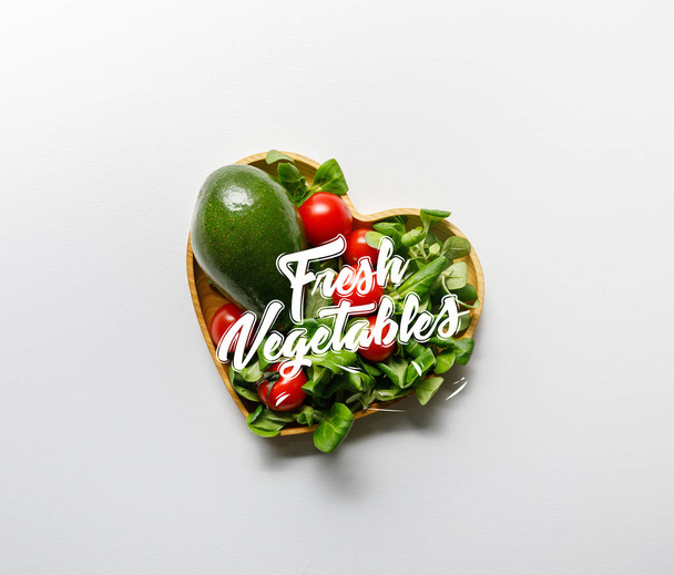 top view of fresh green vegetables in heart shaped bowl on white background with fresh vegetables lettering - Fotó, kép