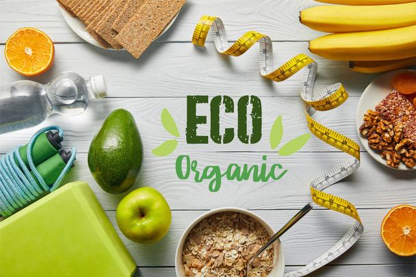 Top zicht op dieetvoeding in de buurt van meetlint en sportuitrusting op houten witte achtergrond met Eco organische belettering - Foto, afbeelding