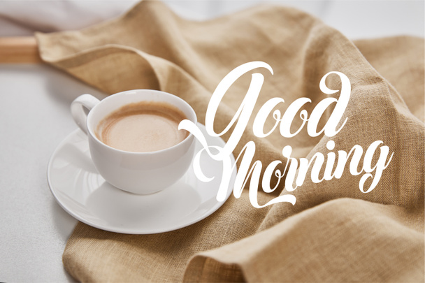 primer plano vista de café en taza blanca en platillo cerca de servilleta beige con buena ilustración mañana
 - Foto, Imagen