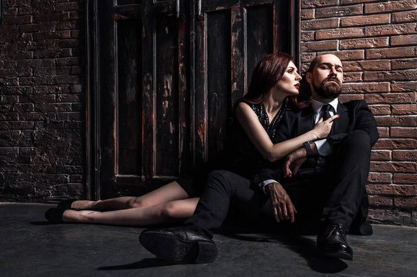 stylish and richly couple hugging while sitting on floor near brick wall  - Foto, immagini