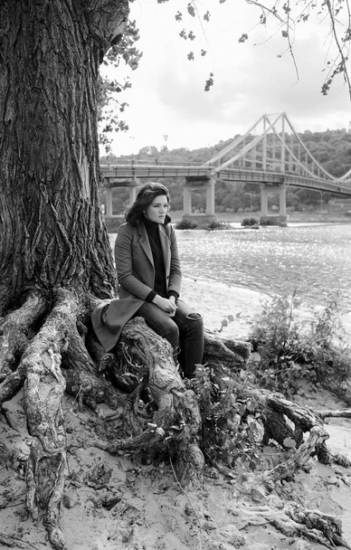 молодая красивая брюнетка депрессивная грустная женщина на берегу реки в городе на фоне моста
 - Фото, изображение