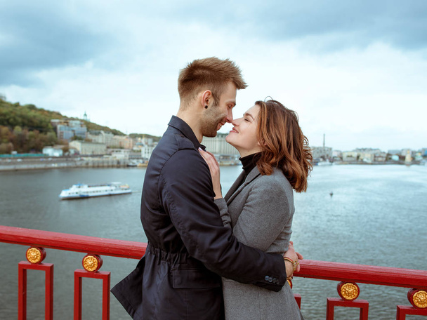 beautiful amazing sweet cheerful young couple (man and woman) standing on bridge by the river on cityscape background. Family, tenderness, dating, urban, love and friendship concept - Foto, imagen