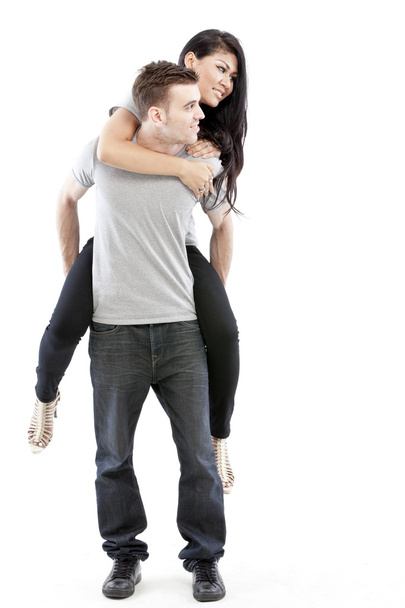 Portrait of a happy young man giving a piggyback ride to her girlfriend against white background - Foto, imagen