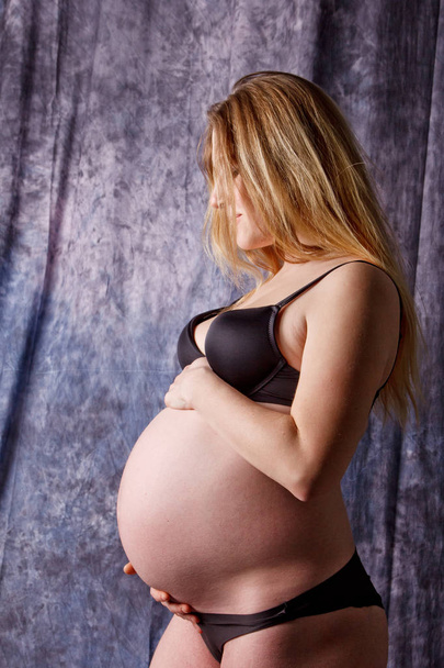 A pregnant woman in lingerie with a big belly in the ninth month of pregnancy is hugging her abdomen. in anticipation of childbirth - Foto, immagini