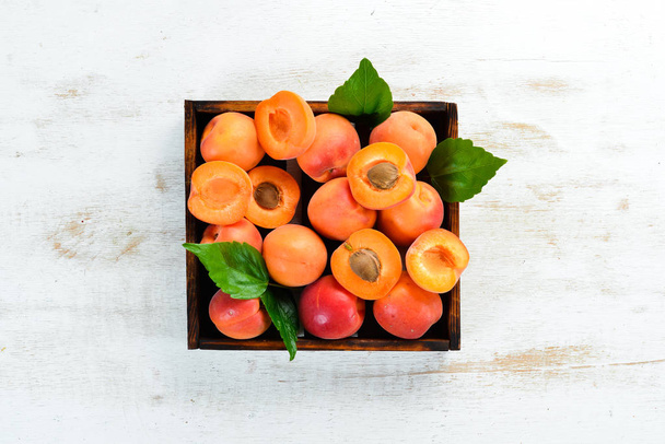 Fresh apricots with green leaves in a box. Rustic style. Top view. Free space for your text. - Фото, зображення