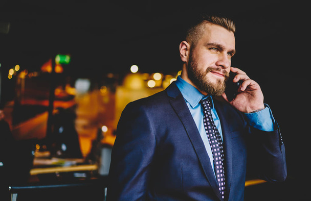 Caucasian bearded entrepreneur calling on smartphone device and talking with business partner.Caucasian confident proud ceo dressed in formal wear communicating on modern mobile phone - Foto, Imagen