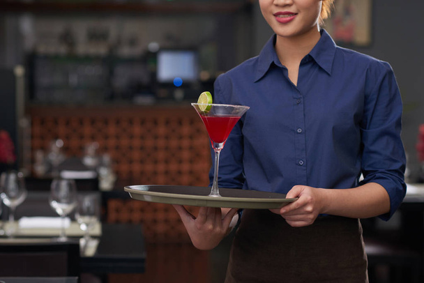 Обрізане зображення офіціантки, що тримає лоток з коктейлем на ньому
 - Фото, зображення
