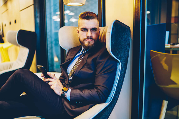 Portrait of confident businessman dressed in formal wear looking at camera while sitting in comfortable chair in office interior. Confident in future corporate entrepreneur feeling thoughtful - Foto, afbeelding
