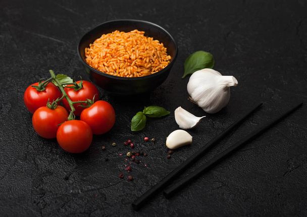 Black plate bowl of rice with tomato and basil and garlic and chopsticks on black stone background. Traditional food. - Foto, Imagen