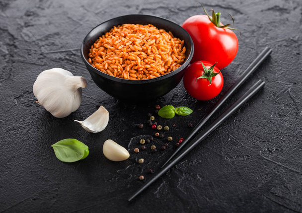 Black plate bowl of rice with tomato and basil and garlic and chopsticks on black stone background. Traditional food. - Foto, Imagem