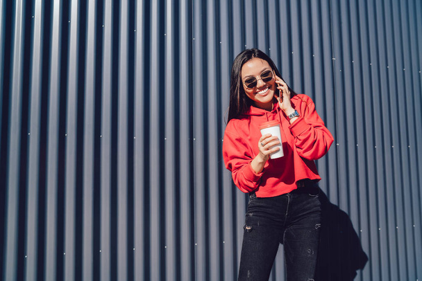 Cheerful female teengaer in stylish sunglasses feeling excited from received good news during positive international smartphone conversation, happy woman laughing while communicate with friend - Foto, afbeelding