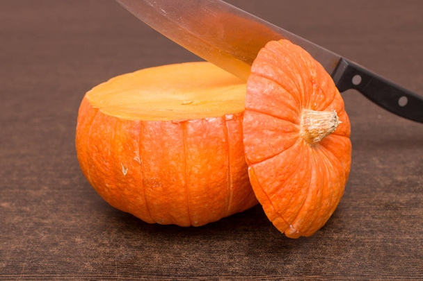 cut orange pumpkin on the wooden brown table with iron knife in this one - Photo, image