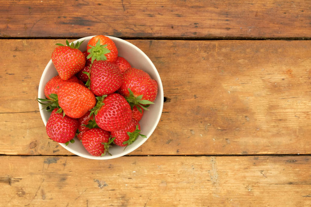 strawberries in a bowl and on a wooden table top - Фото, зображення