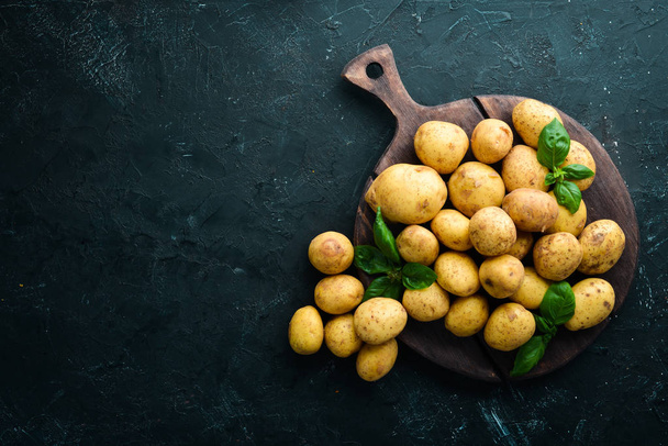 Fresh potatoes on a black background. Organic food. Top view. Free space for text. - Foto, Imagen