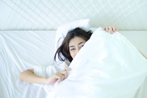 寝室で寝ている美しい女性ベッドにうつ伏せに横たわる女性パジャマを着た女の子は、朝、白い部屋のベッドで眠ります。暖かいトーン. - 写真・画像